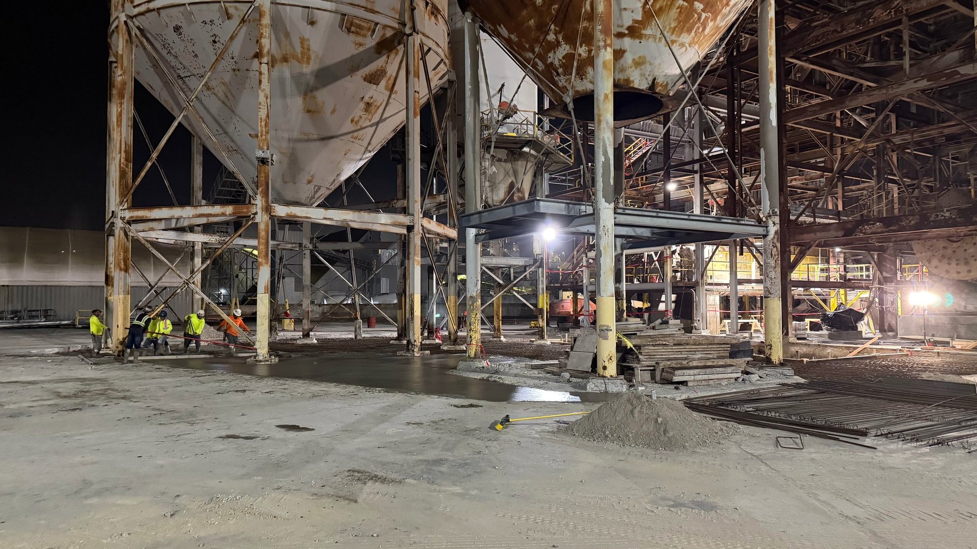 Industrial nighttime scene of a metal storage structure with large cylindrical tanks and support beams under construction lighting