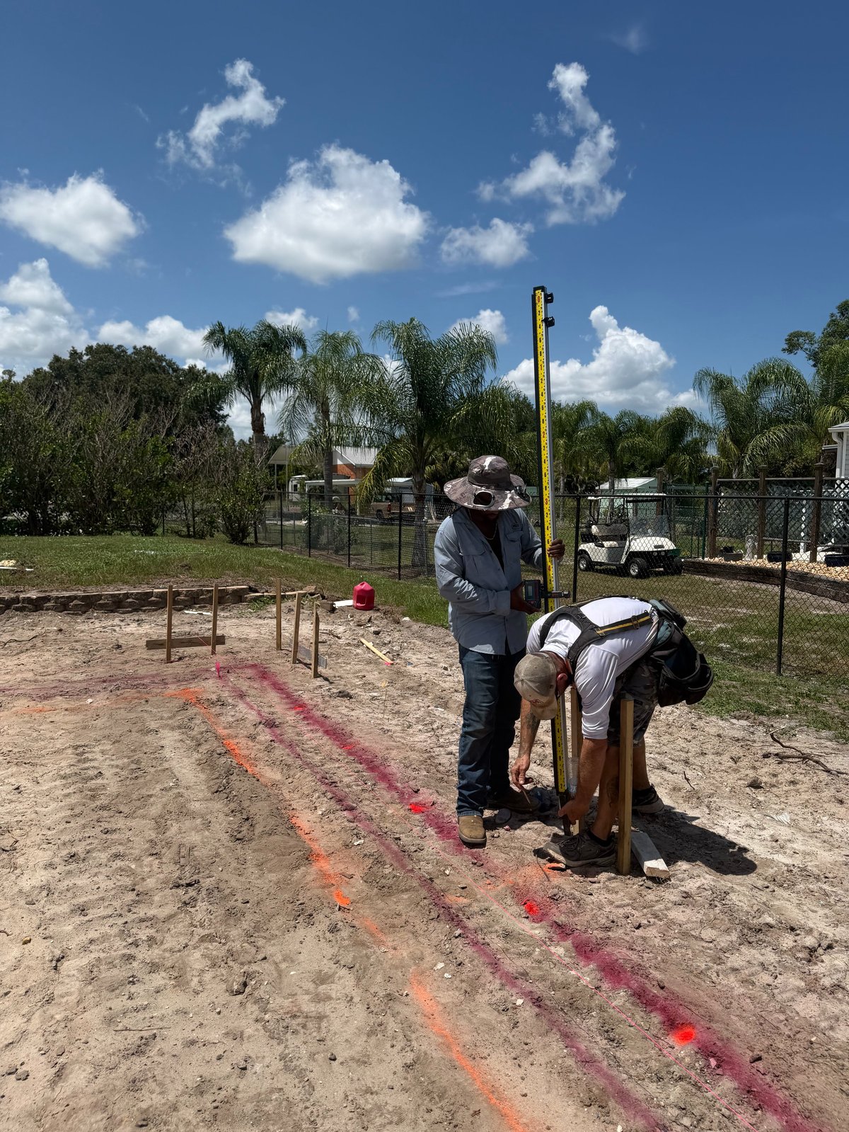 Trainer instructing a horse and rider on marked ground at an equestrian facility with palm trees and blue sky