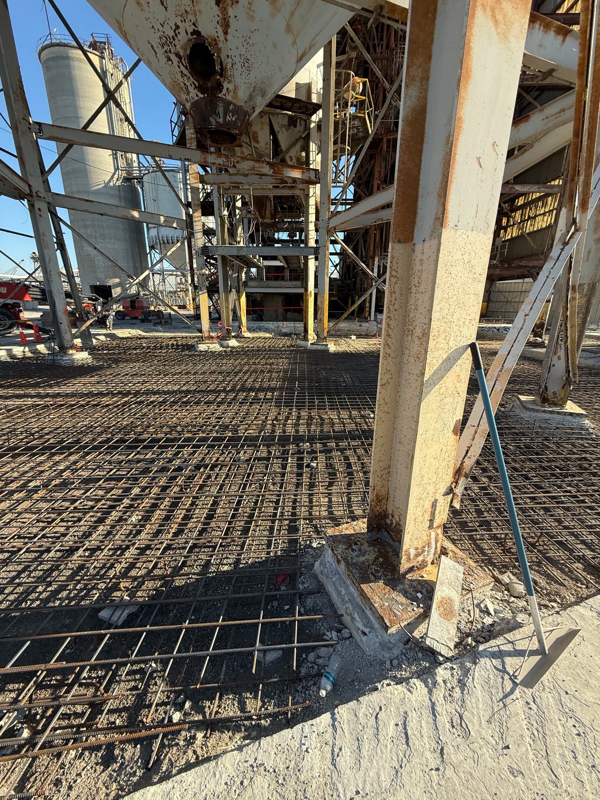 Industrial facility with concrete posts, metal grating floor, and storage silo in background under clear sky